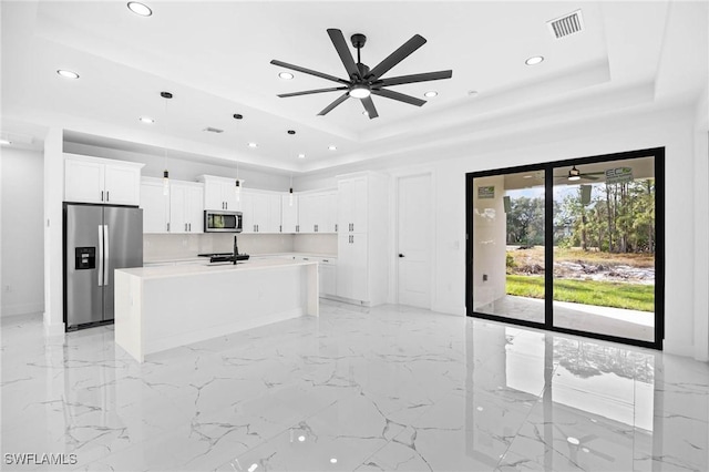 kitchen with a raised ceiling, white cabinetry, a center island with sink, and appliances with stainless steel finishes