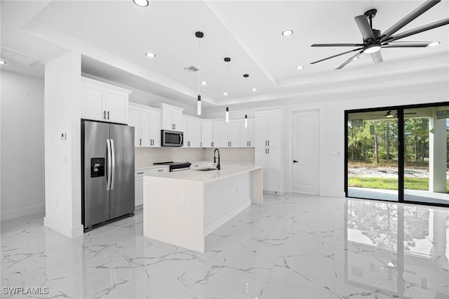 kitchen with decorative light fixtures, stainless steel appliances, white cabinetry, and an island with sink