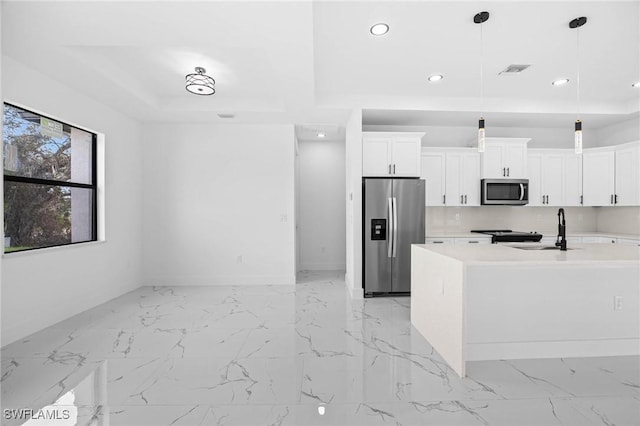 kitchen featuring white cabinetry, sink, hanging light fixtures, stainless steel appliances, and a kitchen island with sink