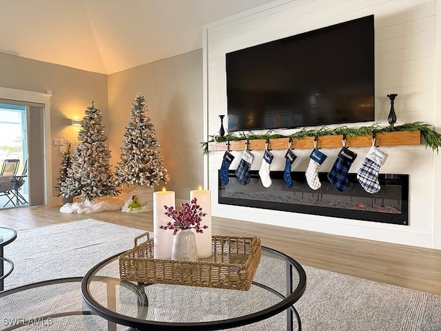 living room featuring a glass covered fireplace, vaulted ceiling, and wood finished floors