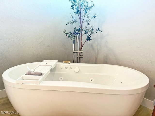 full bath featuring a freestanding bath, a textured wall, and wood finished floors