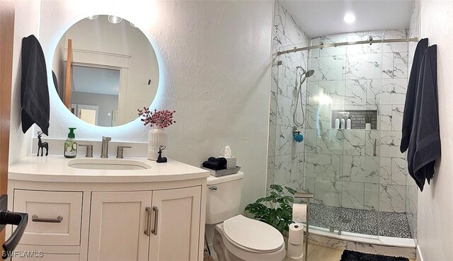 full bathroom featuring a marble finish shower, a textured wall, vanity, and toilet