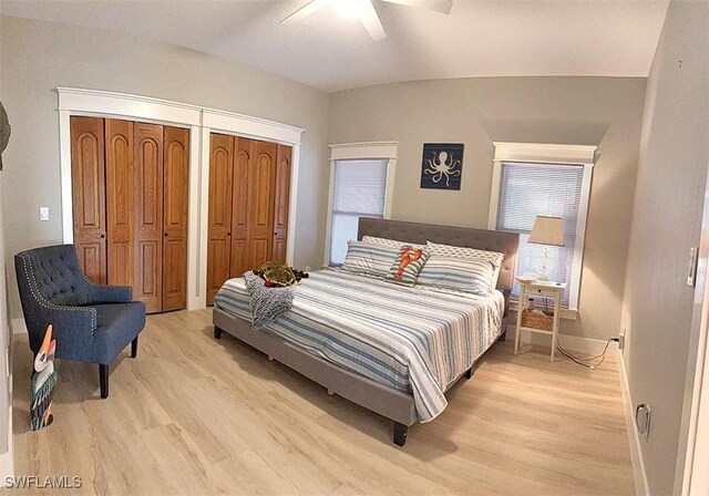 bedroom with light wood-type flooring, ceiling fan, baseboards, and multiple closets