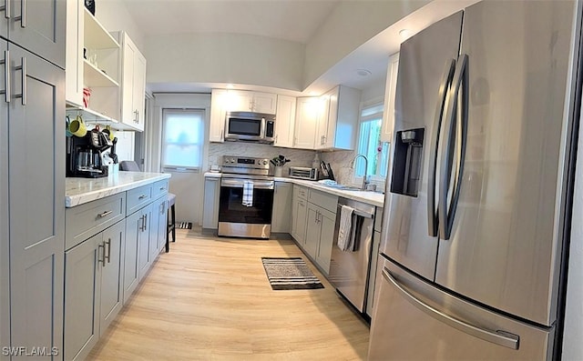 kitchen featuring gray cabinetry, a sink, appliances with stainless steel finishes, light wood-type flooring, and tasteful backsplash