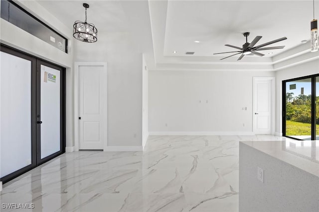 foyer featuring french doors, ceiling fan with notable chandelier, and a tray ceiling