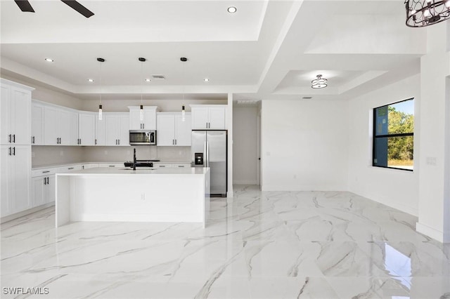 kitchen with ceiling fan, stainless steel appliances, an island with sink, decorative light fixtures, and white cabinets