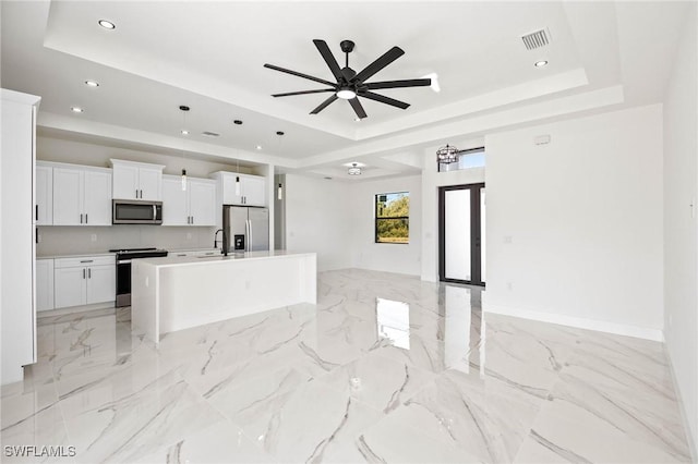 kitchen featuring a tray ceiling, white cabinetry, a center island with sink, and appliances with stainless steel finishes