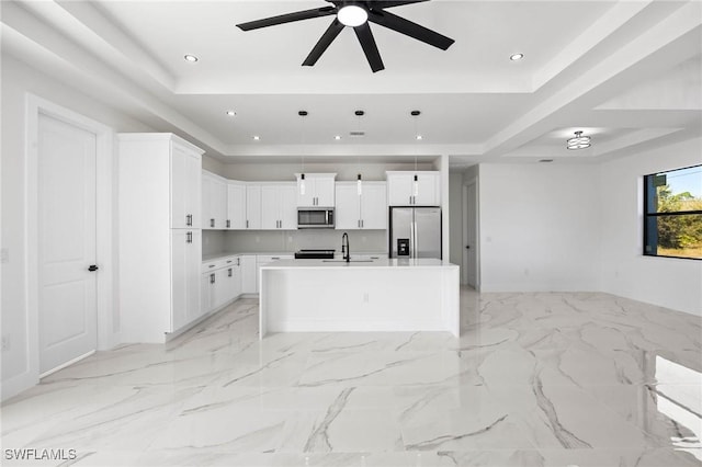 kitchen with pendant lighting, a kitchen island with sink, white cabinets, a raised ceiling, and stainless steel appliances