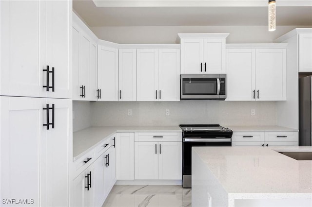 kitchen featuring light stone countertops, white cabinets, hanging light fixtures, and appliances with stainless steel finishes