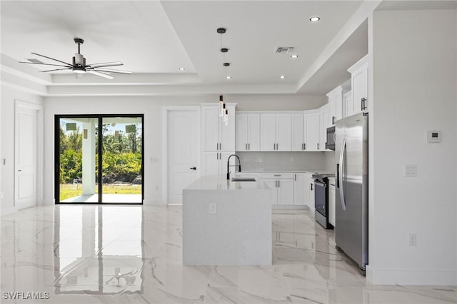 kitchen featuring white cabinetry, a kitchen island with sink, appliances with stainless steel finishes, and a tray ceiling