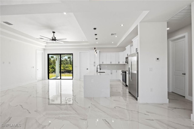 kitchen with white cabinets, sink, ceiling fan, an island with sink, and a tray ceiling