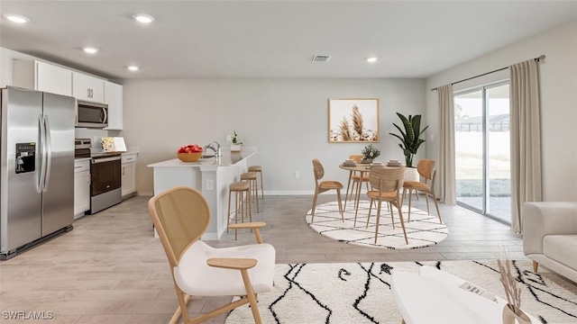 kitchen with white cabinets, appliances with stainless steel finishes, a breakfast bar, and light hardwood / wood-style floors