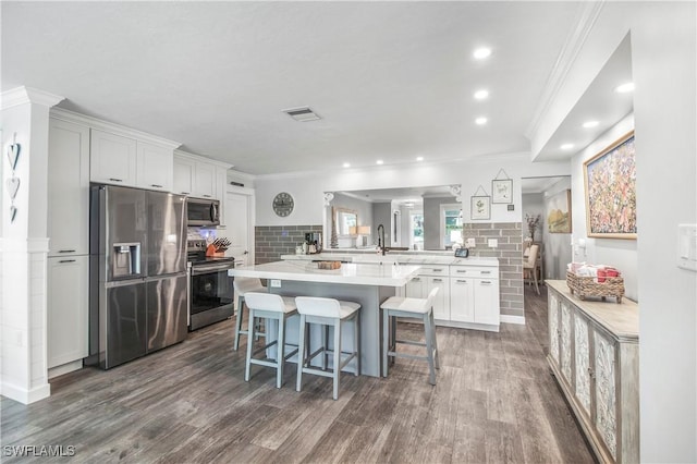 kitchen with kitchen peninsula, dark hardwood / wood-style flooring, a breakfast bar, stainless steel appliances, and white cabinets