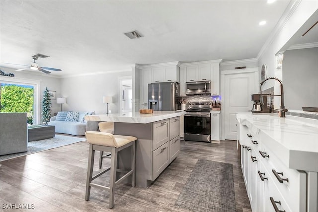 kitchen with a breakfast bar, stainless steel appliances, dark wood-type flooring, white cabinetry, and a kitchen island