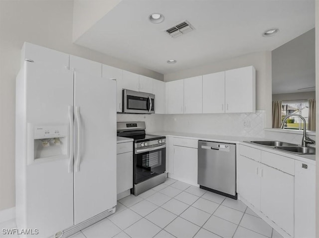 kitchen featuring decorative backsplash, stainless steel appliances, sink, white cabinets, and light tile patterned flooring