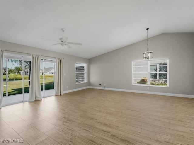 empty room with ceiling fan with notable chandelier, light hardwood / wood-style floors, and vaulted ceiling