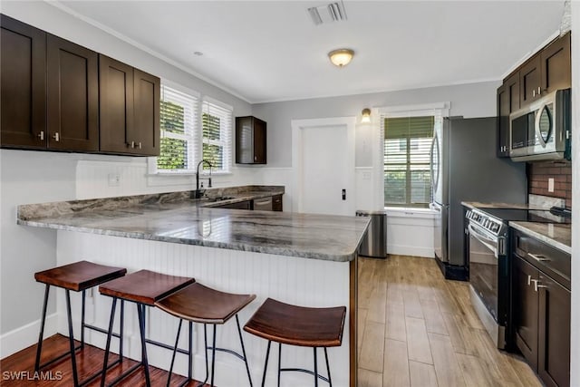 kitchen featuring a breakfast bar, dark brown cabinets, kitchen peninsula, and appliances with stainless steel finishes