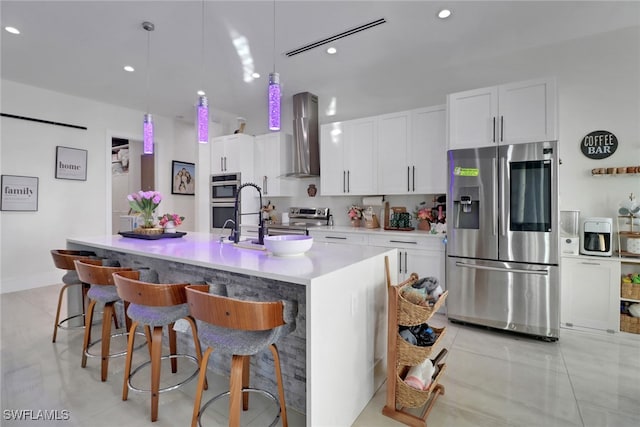 kitchen with white cabinetry, a center island with sink, stainless steel appliances, and wall chimney range hood