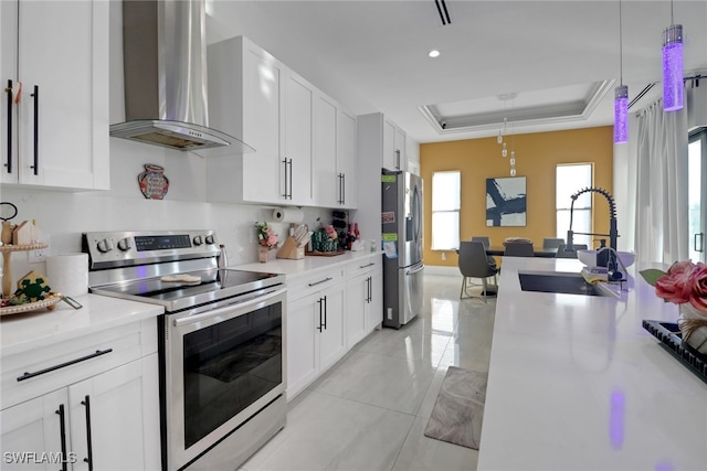 kitchen with appliances with stainless steel finishes, sink, wall chimney range hood, pendant lighting, and white cabinets