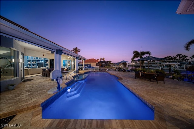 pool at dusk with pool water feature and a patio