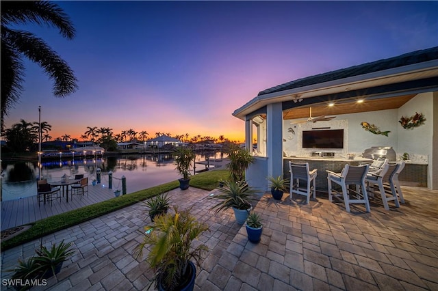 patio terrace at dusk featuring ceiling fan, an outdoor bar, and an outdoor kitchen