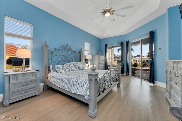 bedroom with access to exterior, light hardwood / wood-style floors, ceiling fan, and a tray ceiling