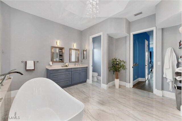 bathroom with a bathing tub, vanity, a notable chandelier, and toilet