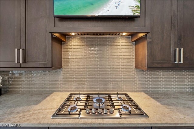 kitchen with light stone countertops, dark brown cabinetry, backsplash, and stainless steel gas cooktop