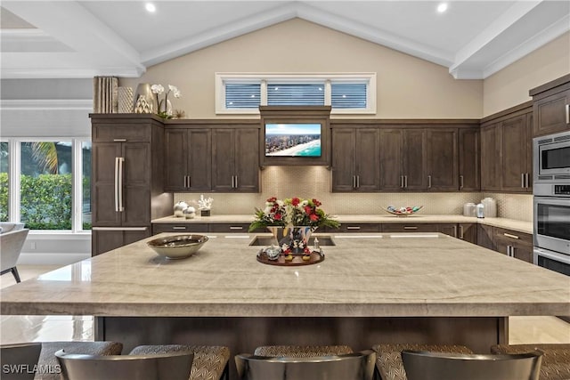 kitchen with a center island with sink, a kitchen breakfast bar, vaulted ceiling, built in appliances, and decorative backsplash