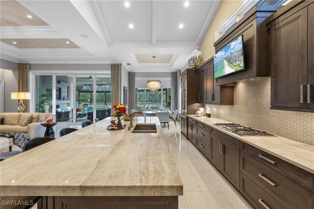 kitchen featuring a large island, light stone counters, backsplash, a chandelier, and stainless steel gas stovetop