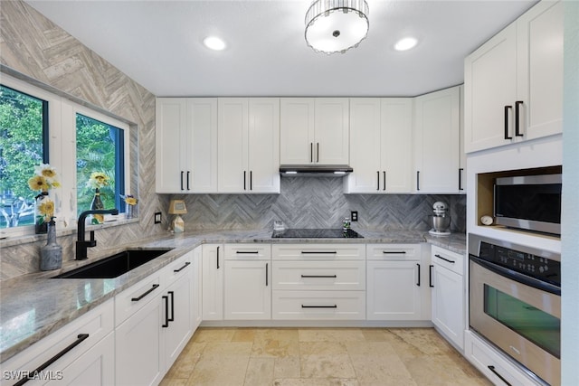 kitchen with sink, stainless steel appliances, light stone counters, decorative backsplash, and white cabinets