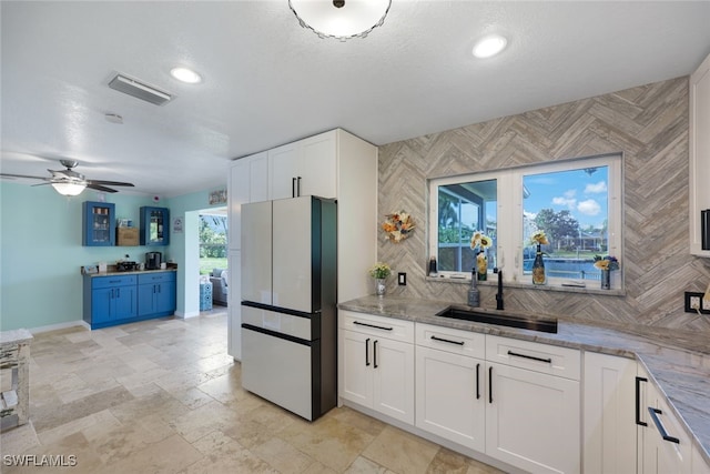 kitchen featuring refrigerator, sink, ceiling fan, light stone countertops, and white cabinetry