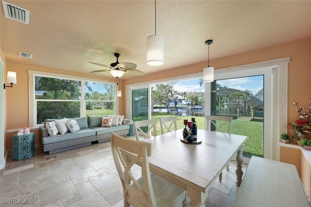 dining space featuring ceiling fan, a water view, and a textured ceiling