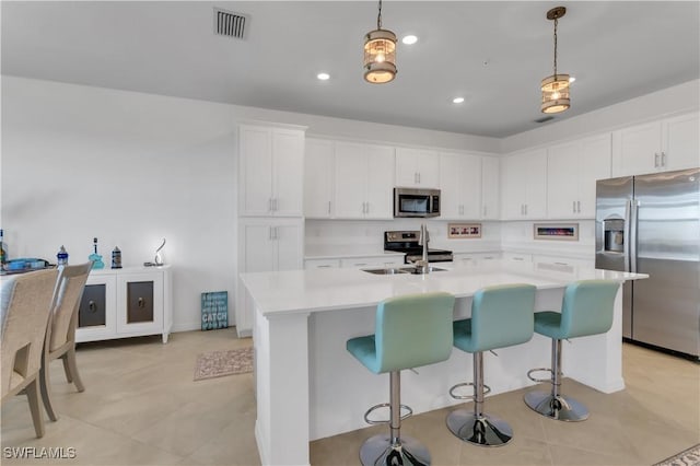 kitchen with pendant lighting, stainless steel appliances, white cabinetry, and an island with sink