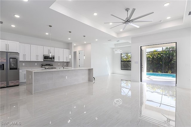 kitchen with white cabinets, appliances with stainless steel finishes, decorative light fixtures, and a tray ceiling