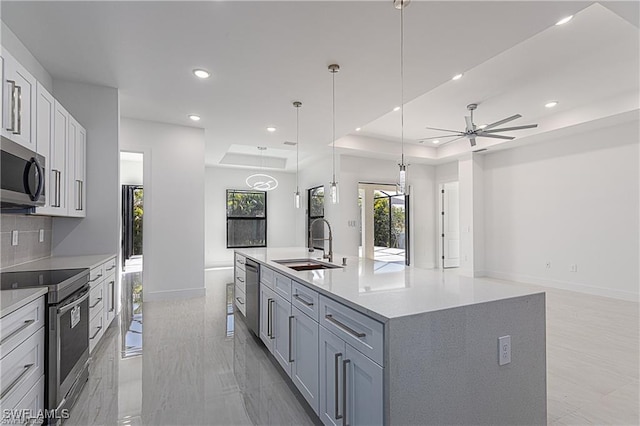 kitchen featuring appliances with stainless steel finishes, a raised ceiling, ceiling fan, sink, and an island with sink