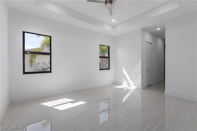 spare room with ceiling fan, a healthy amount of sunlight, and a tray ceiling