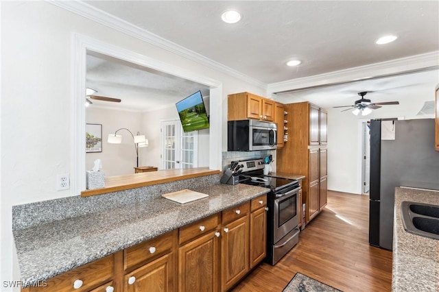 kitchen with crown molding, hardwood / wood-style flooring, ceiling fan, stainless steel appliances, and backsplash