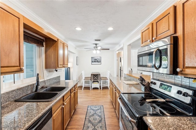 kitchen featuring sink, ornamental molding, stainless steel appliances, and dark stone counters