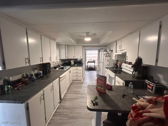 kitchen with white appliances, a raised ceiling, light hardwood / wood-style flooring, ceiling fan, and white cabinetry