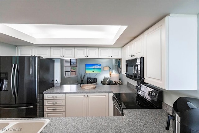 kitchen with black appliances, a raised ceiling, white cabinetry, and a skylight