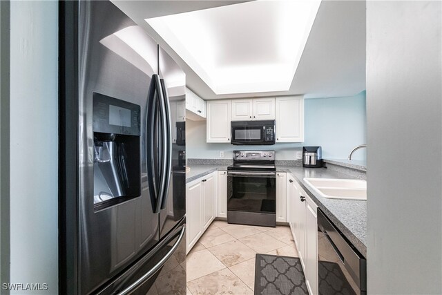 kitchen with sink, light tile patterned floors, a tray ceiling, white cabinets, and appliances with stainless steel finishes