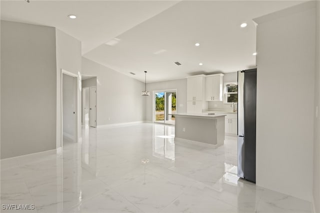 kitchen with backsplash, hanging light fixtures, a kitchen island, white cabinetry, and stainless steel refrigerator