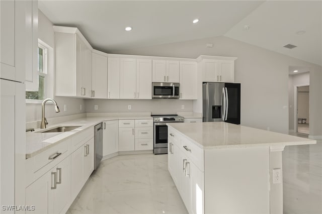 kitchen with white cabinets, sink, vaulted ceiling, appliances with stainless steel finishes, and a kitchen island