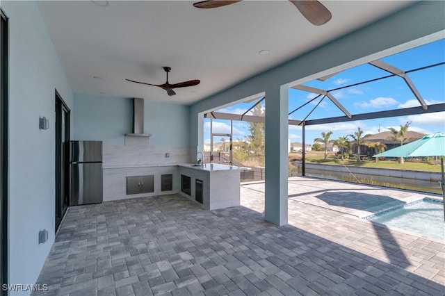 view of patio with ceiling fan, glass enclosure, and sink