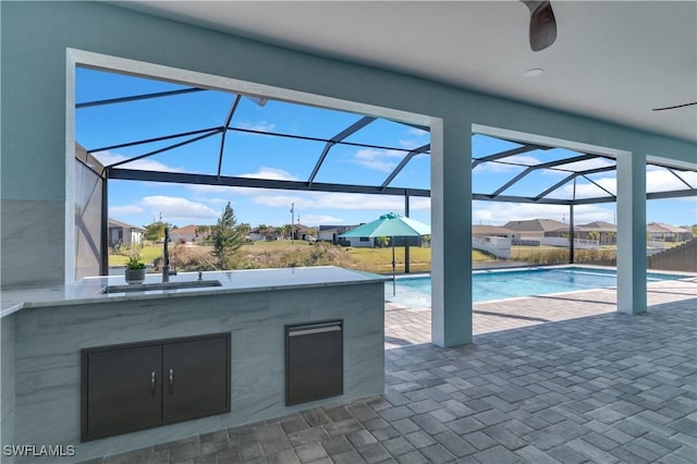 view of swimming pool with an outdoor wet bar, a patio area, ceiling fan, and glass enclosure