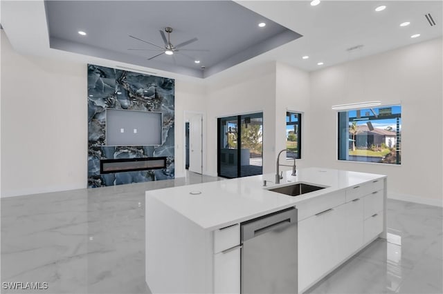 kitchen with a center island with sink, a tray ceiling, sink, white cabinetry, and stainless steel dishwasher