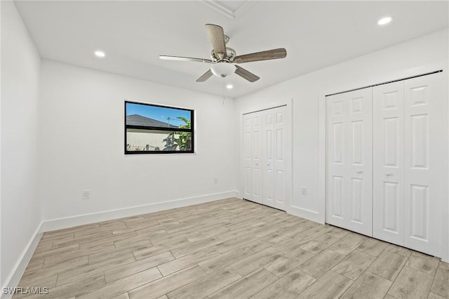 unfurnished bedroom with ceiling fan, light wood-type flooring, and two closets