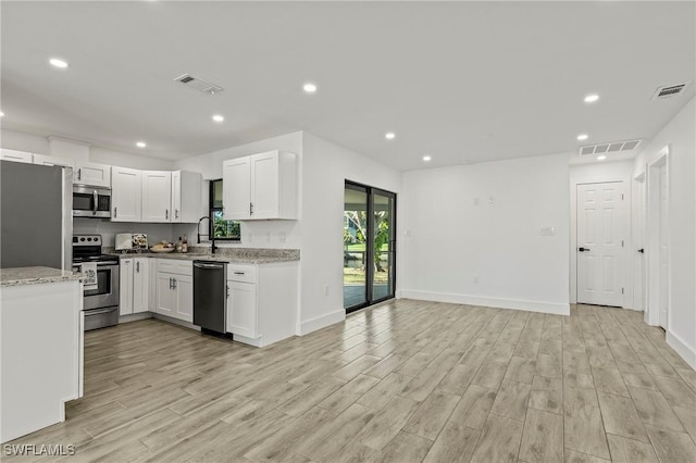 kitchen featuring light stone countertops, light wood-type flooring, stainless steel appliances, sink, and white cabinets