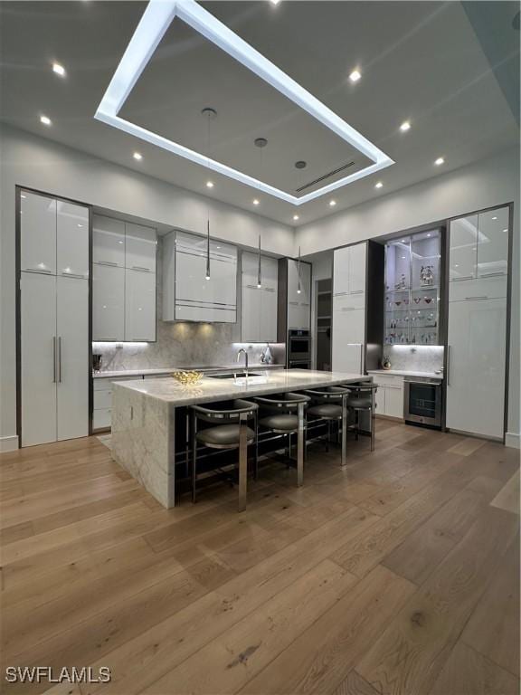 kitchen featuring a kitchen bar, backsplash, a spacious island, wood-type flooring, and white cabinets